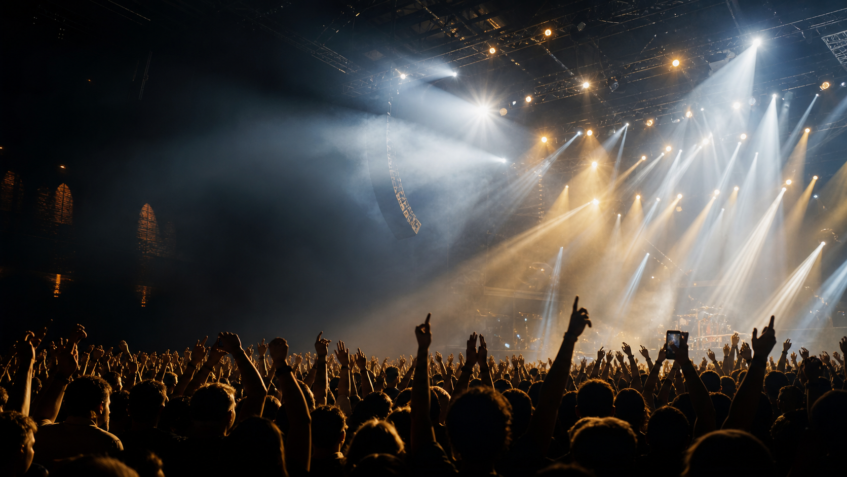 Packed concert crowd under white and brass stage lights